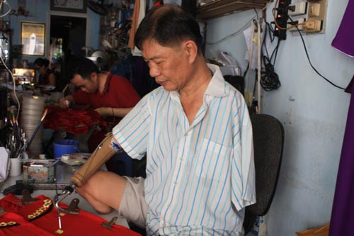 Ông Trần Hùng Bảo miệt mài vẽ hoa trên áo dài thiếu nữ. Ảnh: Nguyễn Đức
